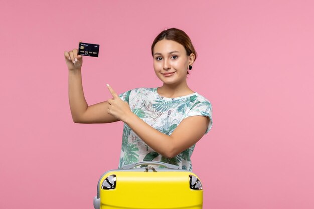 ピンクの壁の飛行機の休暇の飛行航海の女性の休息に黒い銀行カードを保持している正面図若い女性