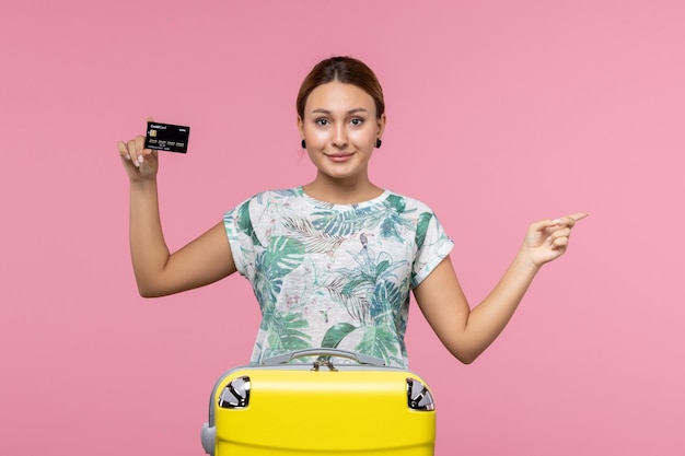 Front view young woman holding black bank card on the pink wall plane vacation flight voyage woman rest