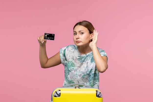 분홍색 벽에 검은색 은행 카드를 들고 있는 젊은 여성의 전면 모습