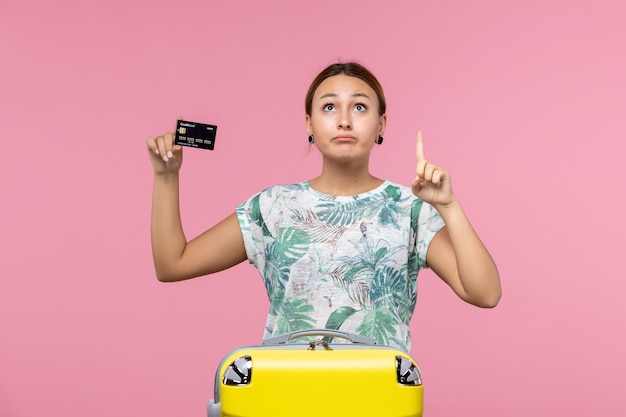 Front view of young woman holding black bank card on pink wall