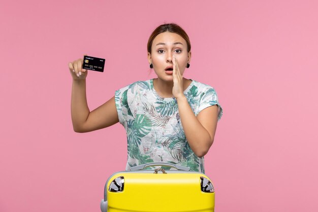 Вид спереди молодой женщины, держащей черную банковскую карту на розовой стене