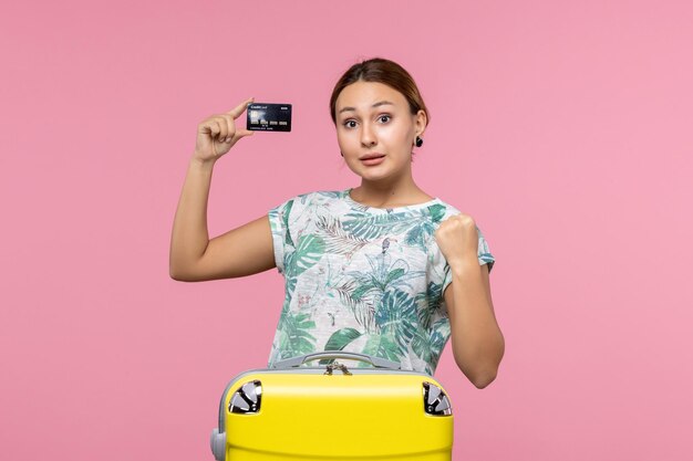 Вид спереди молодой женщины, держащей черную банковскую карту на розовой стене