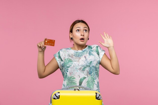 淡いピンクの壁に茶色の銀行カードを保持している若い女性の正面図