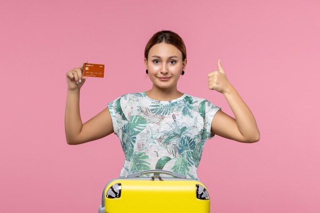 Front view of young woman holding brown bank card on light pink wall