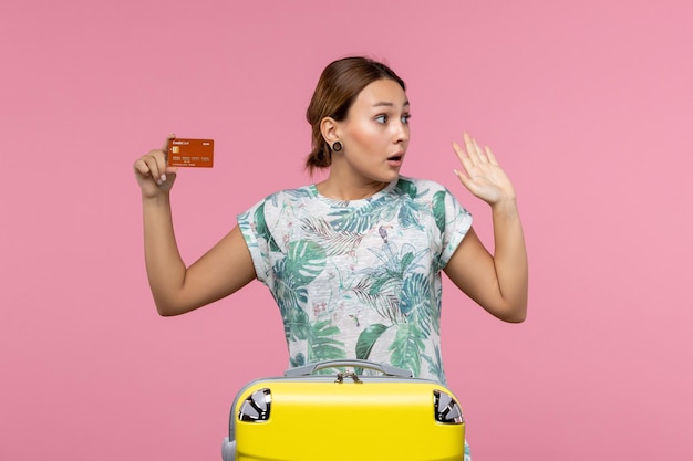 ピンクの壁に茶色の銀行カードを保持している若い女性の正面図