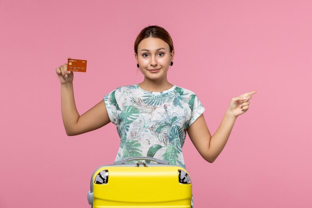 Front view of young woman holding brown bank card on the pink wall