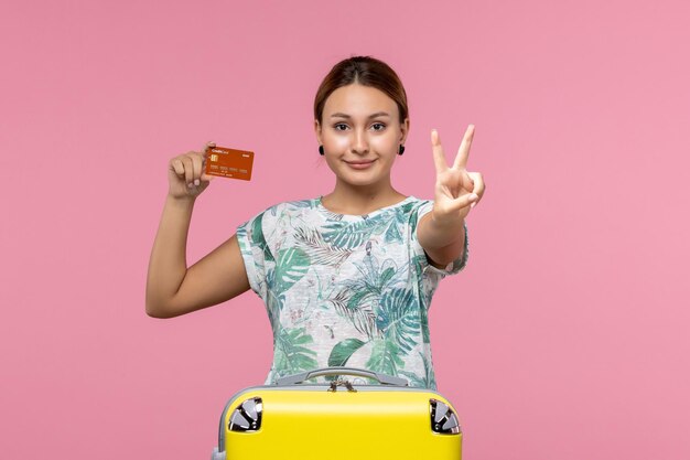 Front view of young woman holding brown bank card and smiling on pink wall