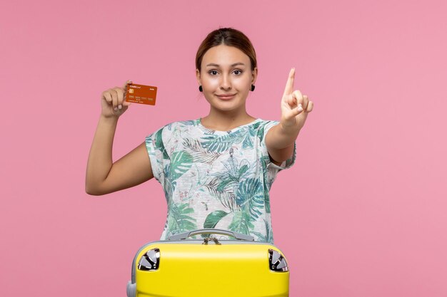 Вид спереди молодой женщины, держащей коричневую банковскую карту с улыбкой на розовой стене