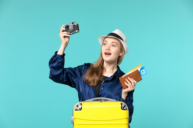 Бесплатное фото Вид спереди молодая женщина, держащая фотоаппарат и билеты на голубом фоне, морское путешествие, путешествие на самолете