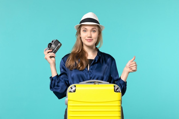 Front view young woman holding camera on the blue background woman journey sea voyage plane