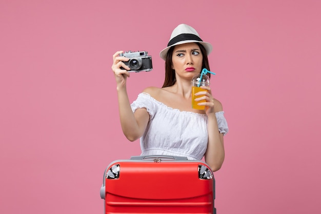 Вид спереди молодая женщина, держащая камеру и коктейль на розовом столе, цветная поездка в отпуск, жара, летнее путешествие