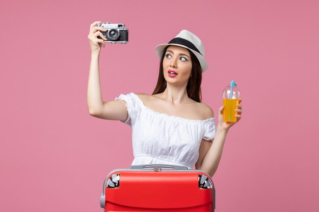 Вид спереди молодая женщина, держащая камеру и коктейль на розовой стене, путешествие, тепло, цвет, отпуск, лето
