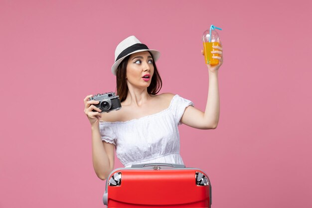 Front view young woman holding camera and cocktail on pink wall vacation trip voyage heat color summer