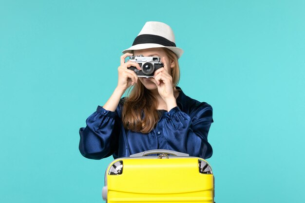 Front view young woman holding camera and taking photos on blue background woman journey sea travelling voyage plane