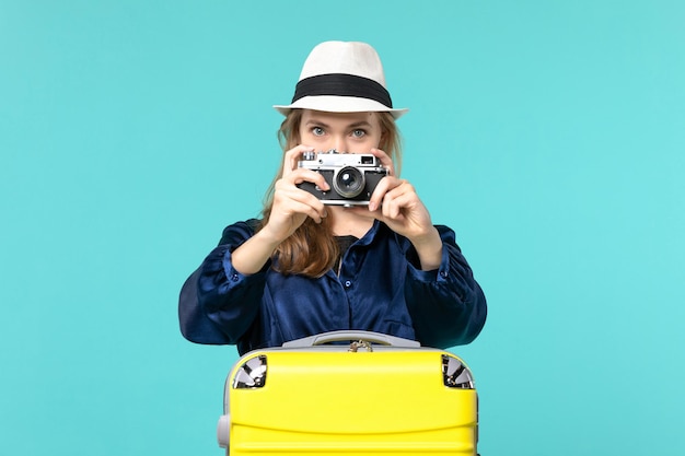 Front view young woman holding camera and taking shot on blue background woman journey sea travelling voyage plane