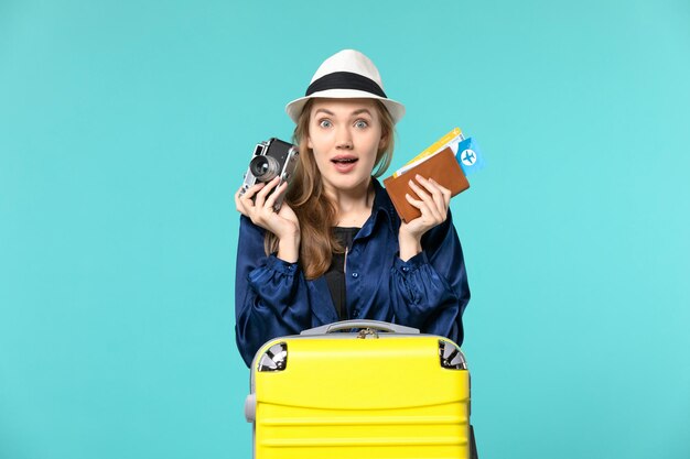 Front view young woman holding camera and tickets on the blue background sea travelling journey plane voyage