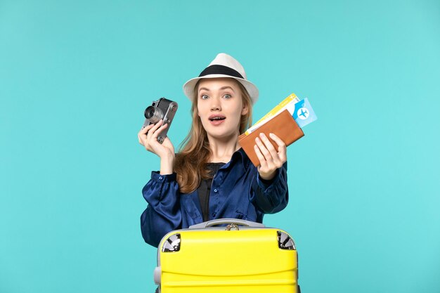 Вид спереди молодая женщина, держащая камеру и билеты на синем фоне, море, путешествие, путешествие, рейс самолет