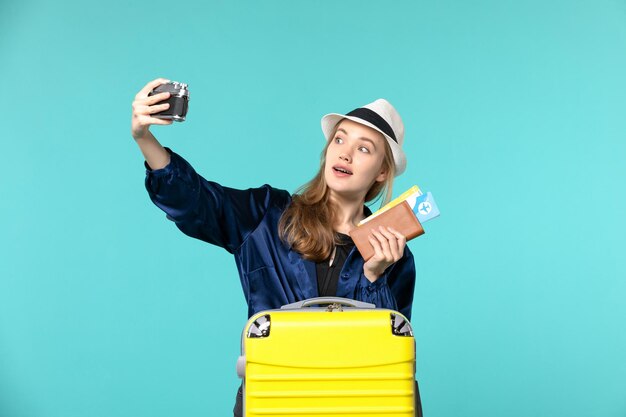 Front view young woman holding camera and tickets on light-blue background sea travelling journey plane voyage