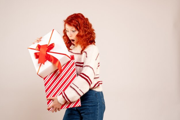 Front view of young woman holding christmas present on white wall