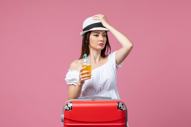 Front view young woman holding cocktail and hat on vacation on pink desk heat summer color vacation trip voyage