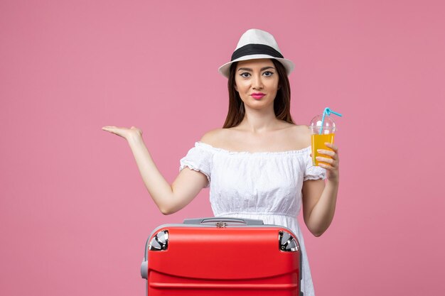 Вид спереди молодая женщина, держащая коктейль с красной сумкой для отпуска на розовой стене, эмоции, отпуск, самолет, путешествие, летнее путешествие