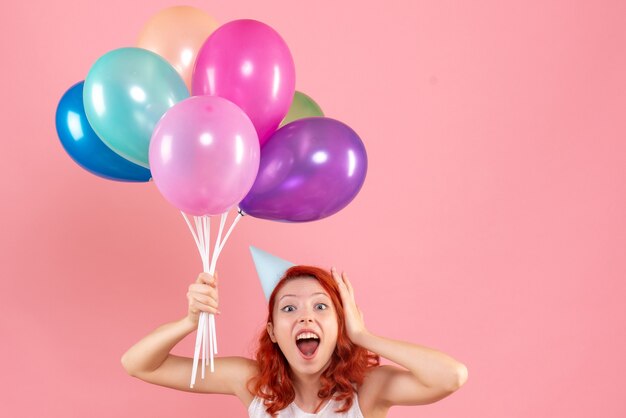 Front view of young woman holding colorful balloons on a pink wall