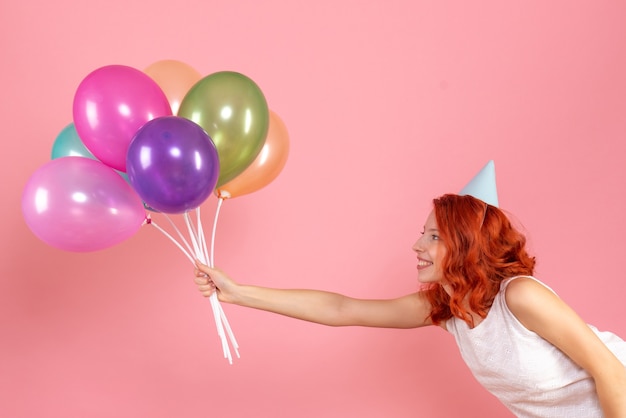 Front view of young woman holding colorful balloons on pink wall
