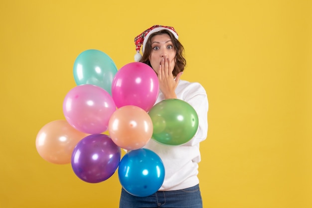 Front view young woman holding colorful balloons with surprised face on yellow