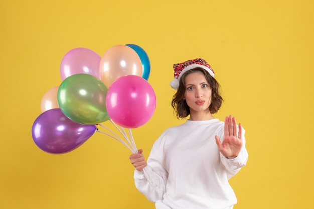 Vista frontale della giovane donna che tiene palloncini colorati sulla parete gialla