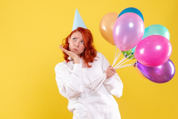 Front view of young woman holding colorful balloons on a yellow wall