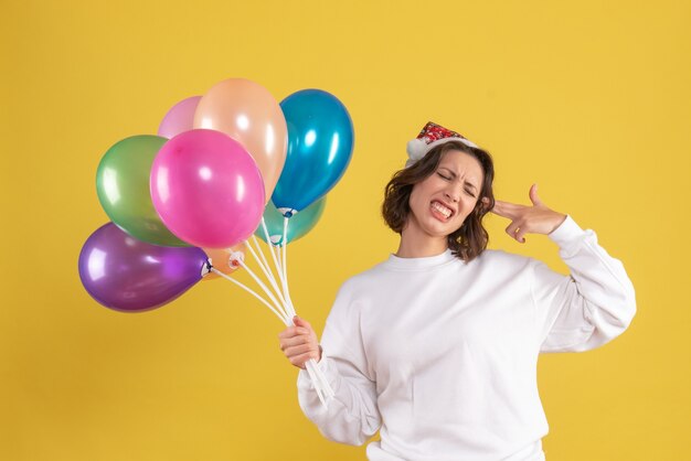 Front view of young woman holding colorful balloons on yellow wall