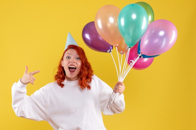 Front view of young woman holding colorful balloons on yellow wall