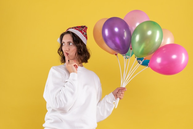 Front view of young woman holding colorful balloons on yellow wall