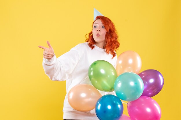 Front view of young woman holding colorful balloons on yellow wall