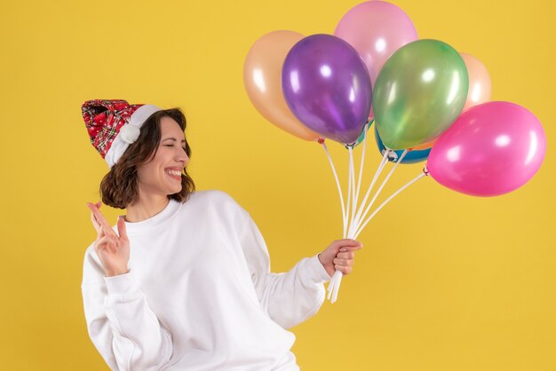 Front view of young woman holding colorful balloons on yellow wall