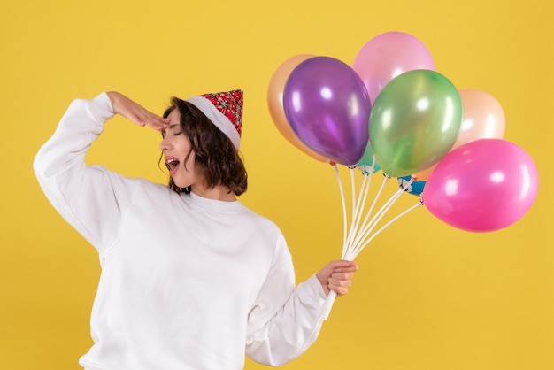 Vista frontale della giovane donna che tiene palloncini colorati sulla parete gialla