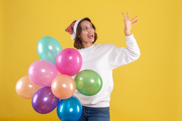 Free photo front view young woman holding colorful balloons on yellow