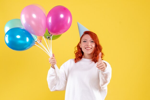 Front view of young woman holding cute colorful balloons on the yellow wall