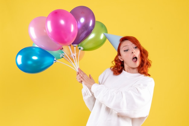 Front view of young woman holding cute colorful balloons on the yellow wall