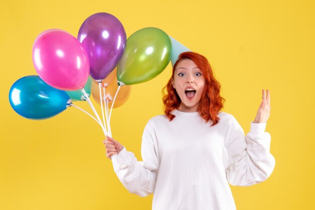 Front view of young woman holding cute colorful balloons on yellow wall