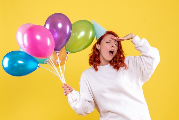 Front view of young woman holding cute colorful balloons on yellow wall