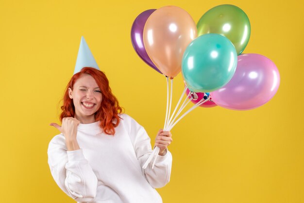 Front view of young woman holding cute colorful balloons on yellow wall