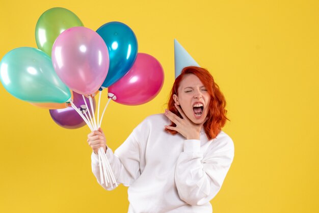 Front view of young woman holding cute colorful balloons on yellow wall