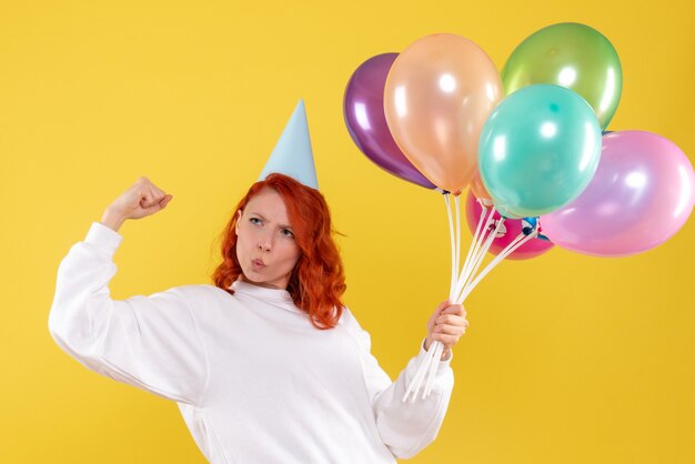 Front view of young woman holding cute colorful balloons on yellow wall