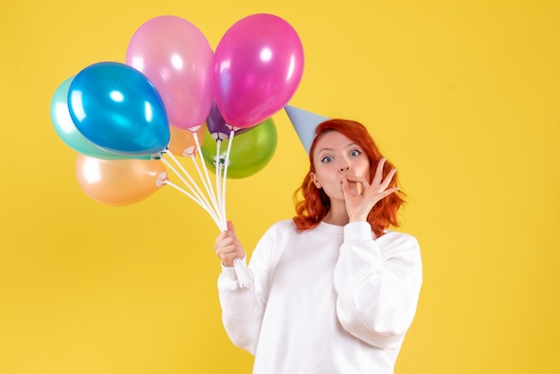 Front view of young woman holding cute colorful balloons on yellow wall