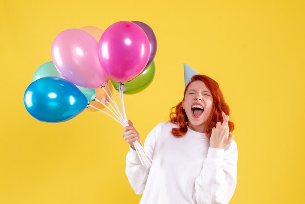 Front view of young woman holding cute colorful balloons on yellow wall