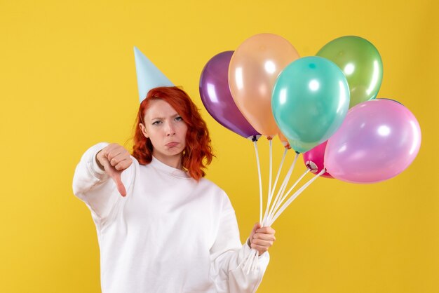 Front view of young woman holding cute colorful balloons on yellow wall