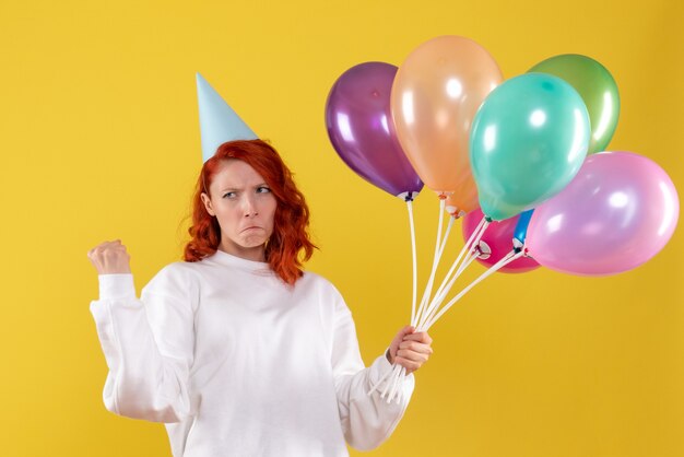 Front view of young woman holding cute colorful balloons on yellow wall