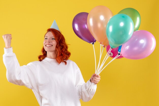 Front view of young woman holding cute colorful balloons on yellow wall