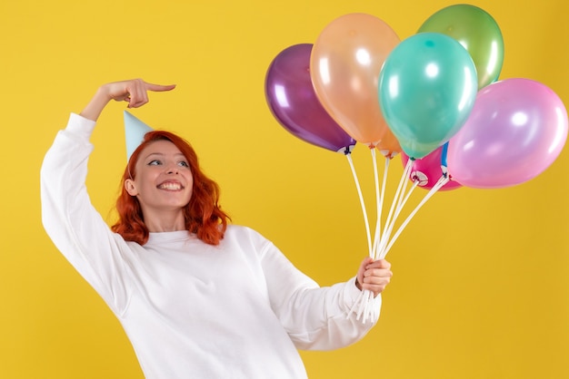 Free photo front view of young woman holding cute colorful balloons on yellow wall